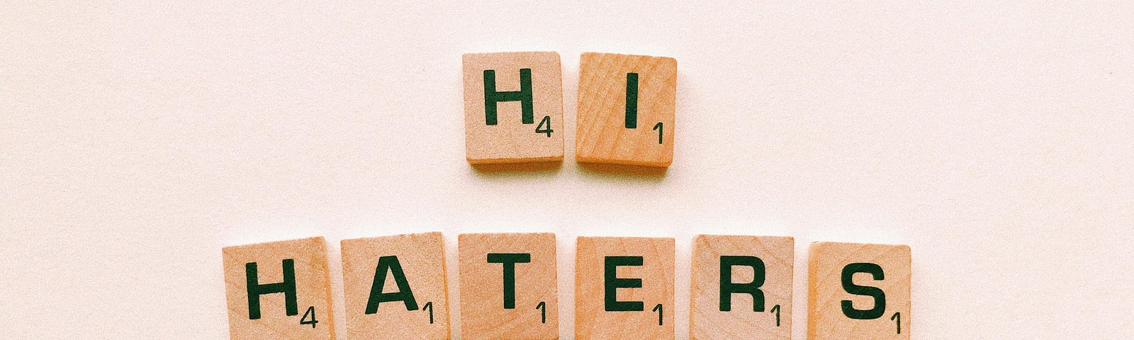 The words “Hi Haters” are spelled out using wooden Scrabble board game pieces.