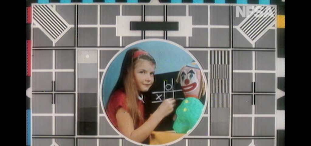 Channel 9 test pattern from the 1970’s, showing a test pattern with a girl holding chalk playing noughts and crosses, next to a clown doll.