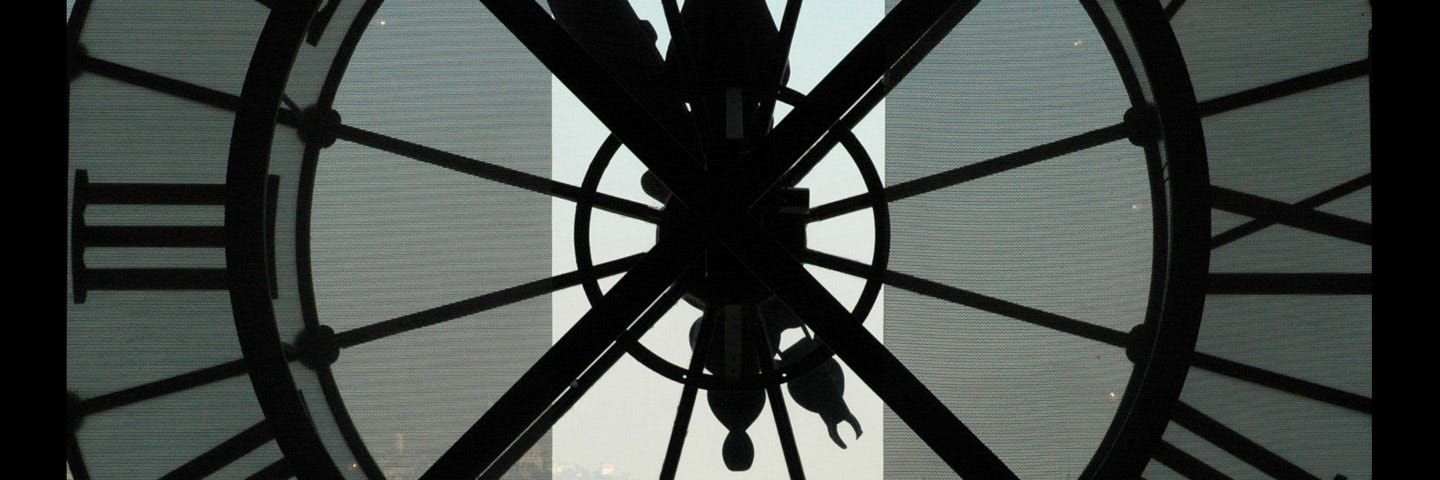 Silhouettes of two people in front of the inside of a large, clear clock overlooking a city.