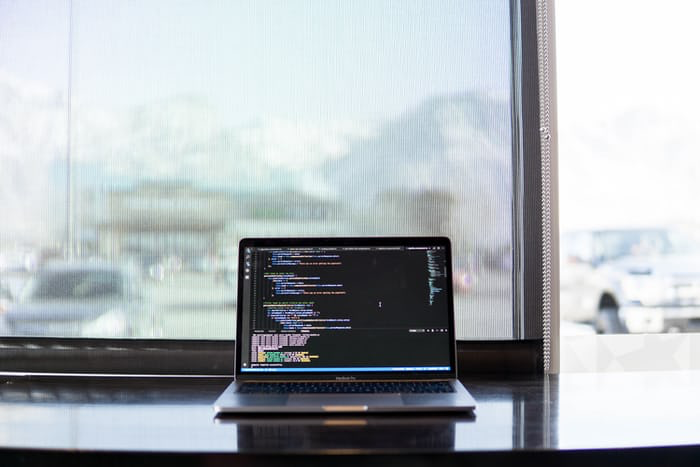 Clean, minimal workspace setup with laptop displaying code in front of a window.