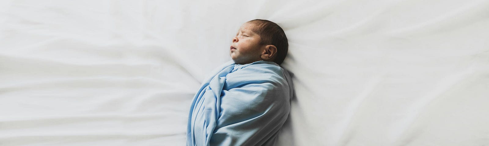 Swaddled newborn baby in a blue blanket on a white sheet