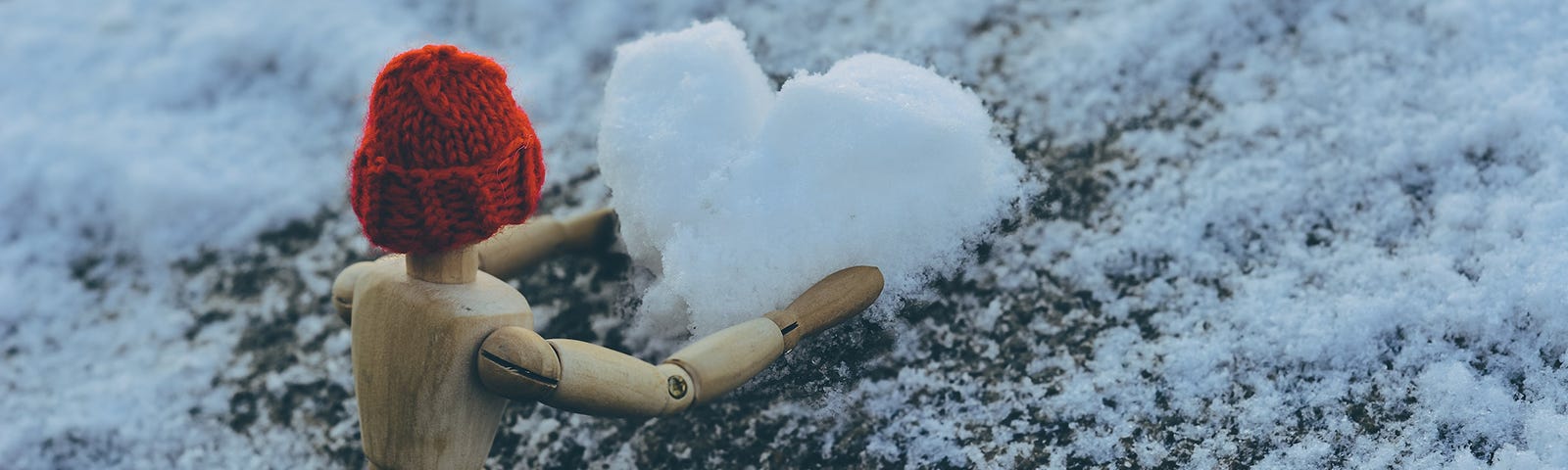 wooden man toy with red hat making a snow heart