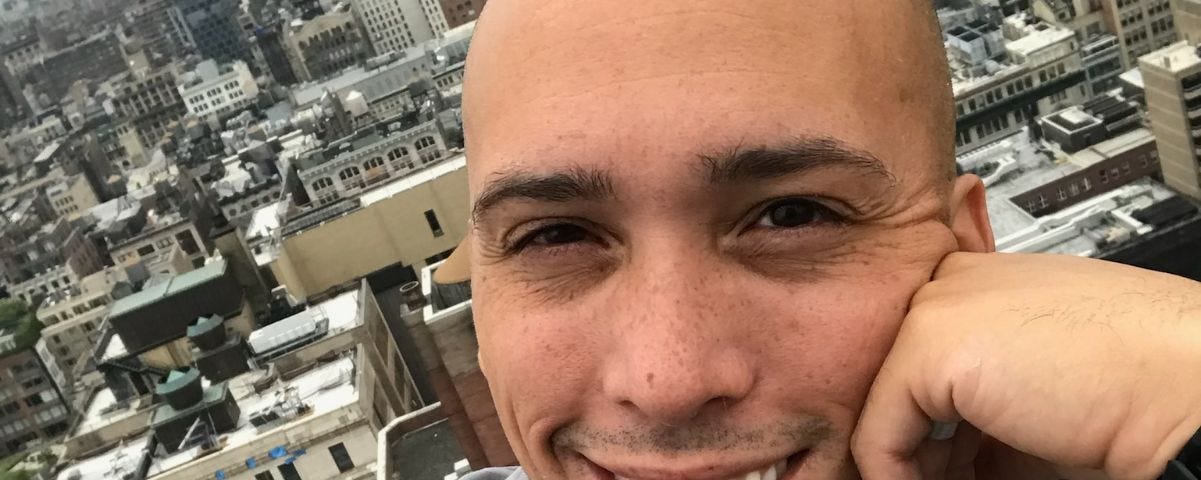 dark-eyed young man with brilliant smile, NY in the background