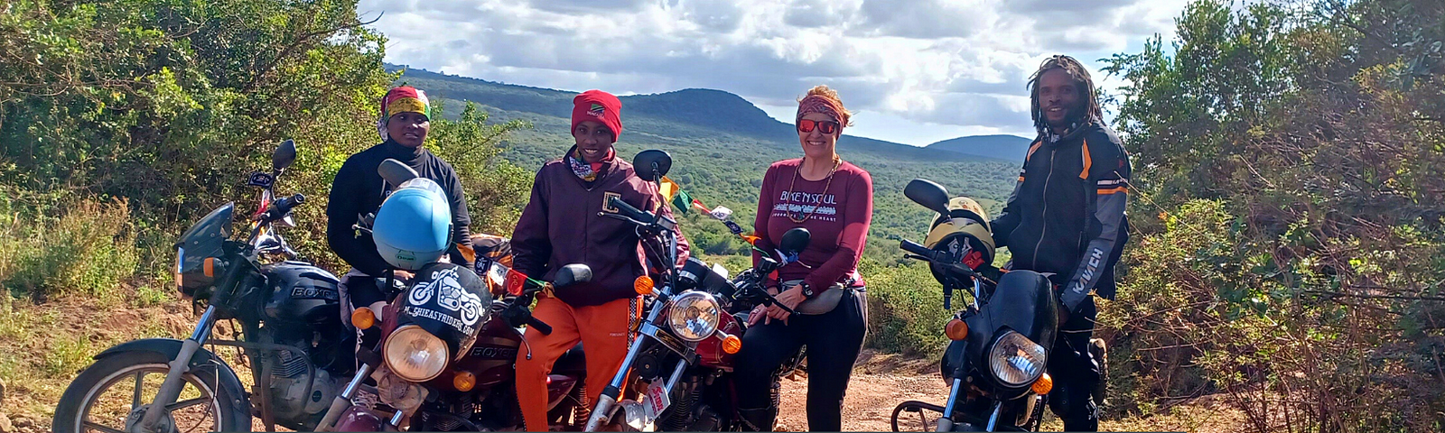 A group of 3 female and one male motorbike riders standing next to their bikes in a bushland in Africa