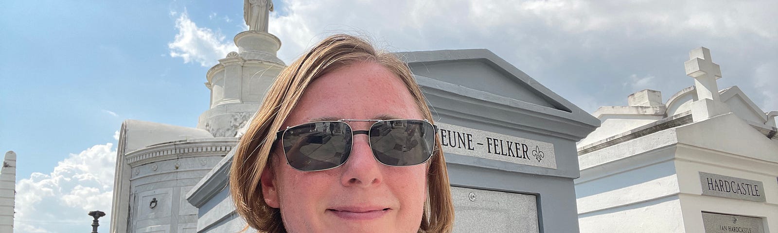 The author is standing in front of some graves in the center of New Orleans. He is wearing sunglasses and a light blue t-shirt.