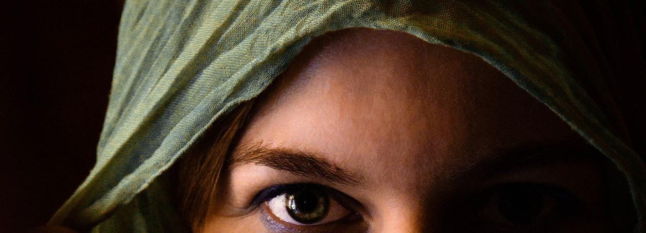 young woman’s face covered with scarf and only revealing one eye