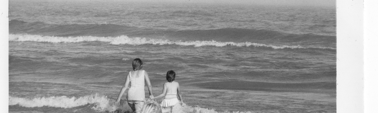 Three girls walking away from the camera and into Lake Michigan (Black and white image from 1970's)