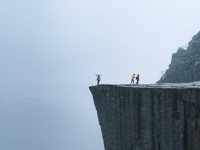 Three figures on top of a huge gray cliff