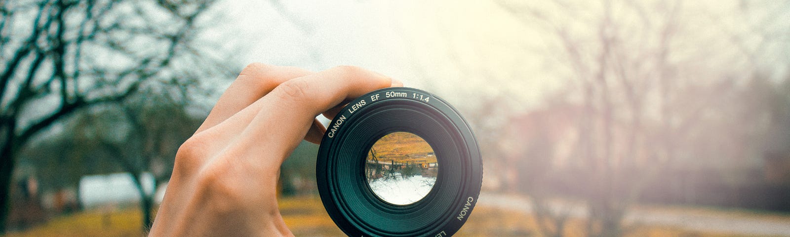 Hand holding a camera lens with woodland in the background.