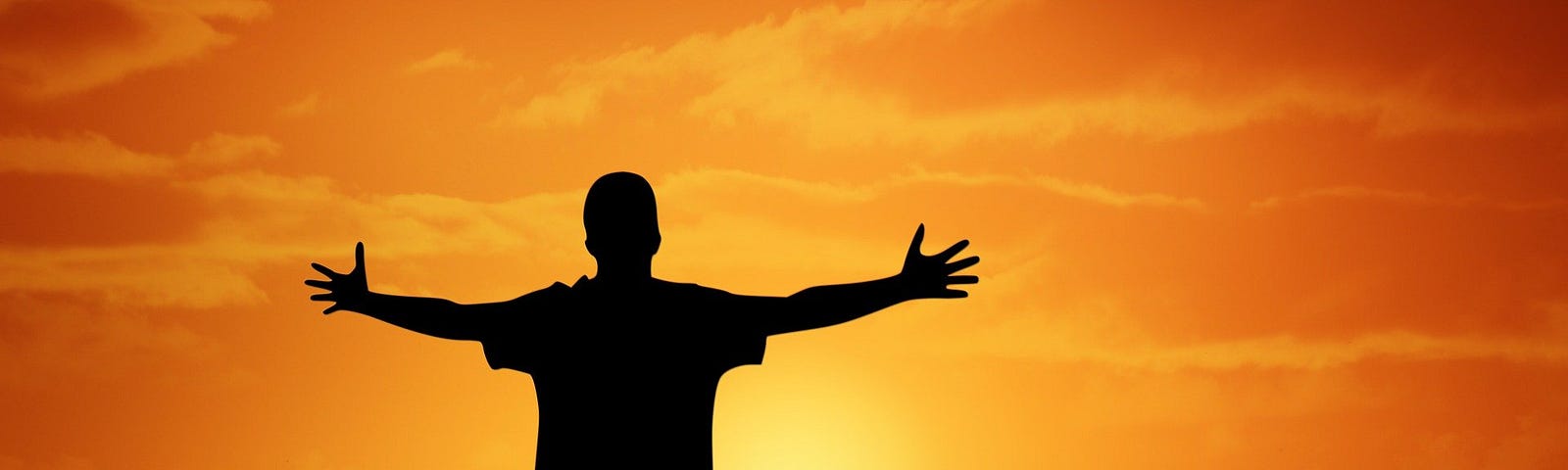 Man outstretching his arms, silhouetted in front of a sunrise.