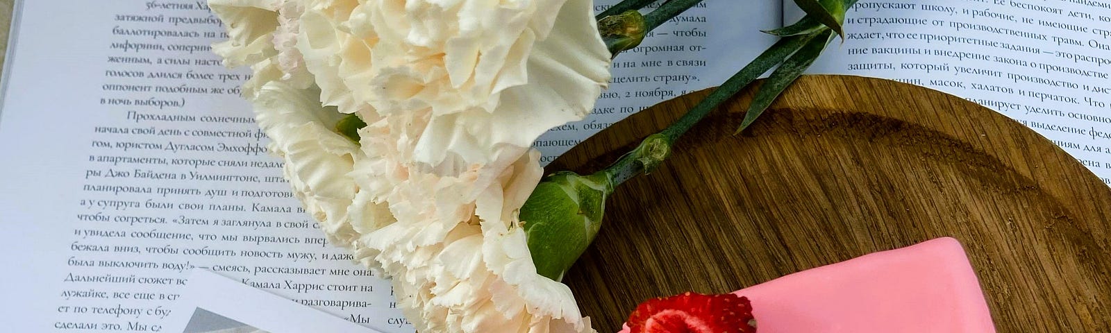 slice of strawberry cake on a circular board with white flowers beside it