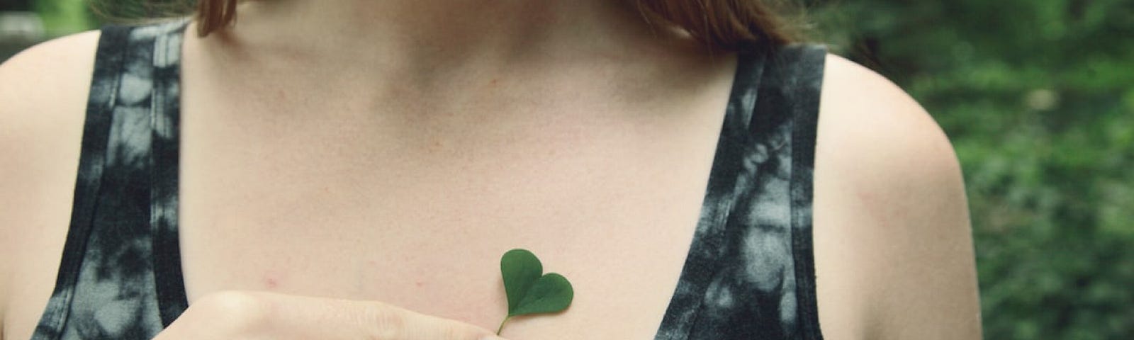Photo of woman’s upper torso holding a heart-shaped clover.