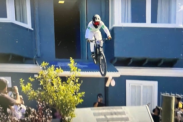 An urban downhill mountain bike racer coming out an elevated door down to a ramp.