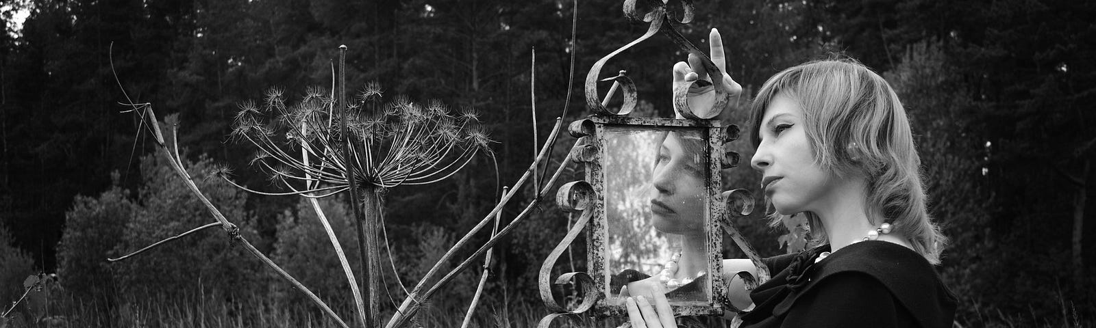 Black and white picture of a women looking into a mirror in the middle of a field