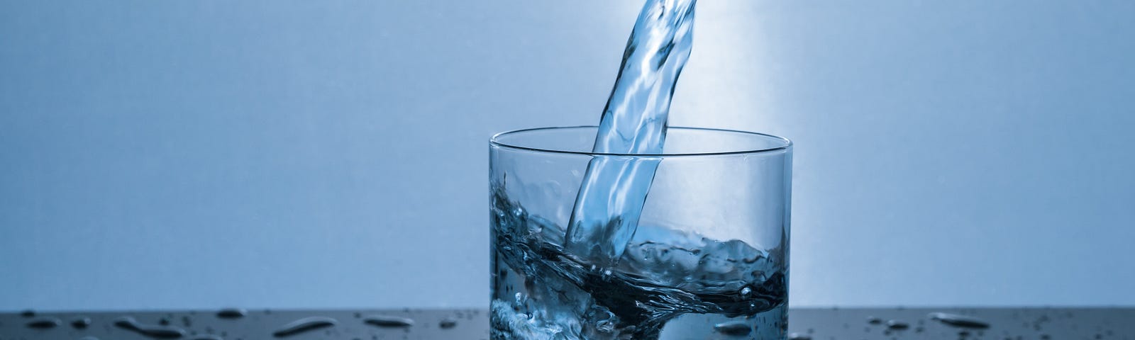 Water being poured into a half-full glass on top of a wet table