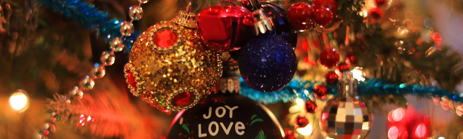 joy, love, peace, believe Christmas ornament on a brightly lit Christmas tree