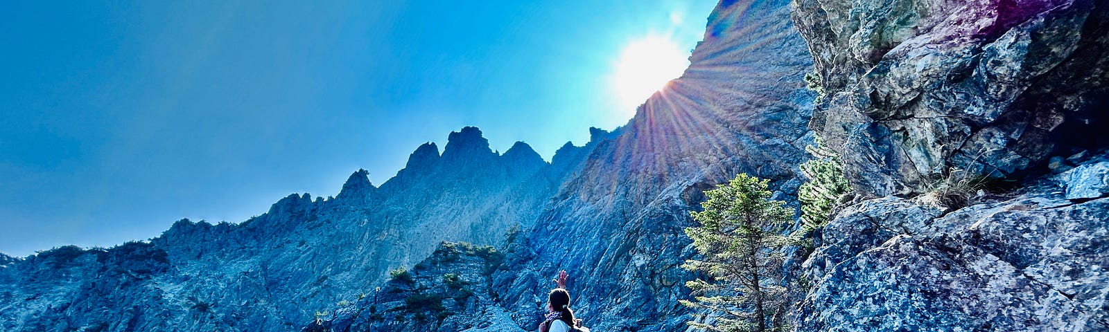 a mountain rocks with a sun shining on top of the rocks and a blue sky with the woman standing on the rocks