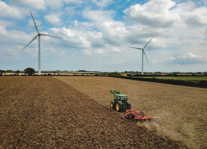 A tractor pulls a plough through a field with wind turbines in the background