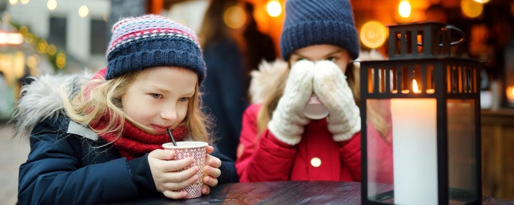 Little girl and mother in holiday stocking caps drinking cocoa.