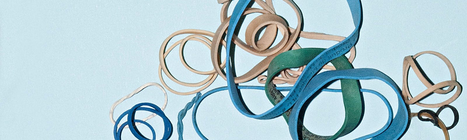 Lots of different circular rubber bands on a bright background thrown on top of each other. Some are twisted, others are nearly round.