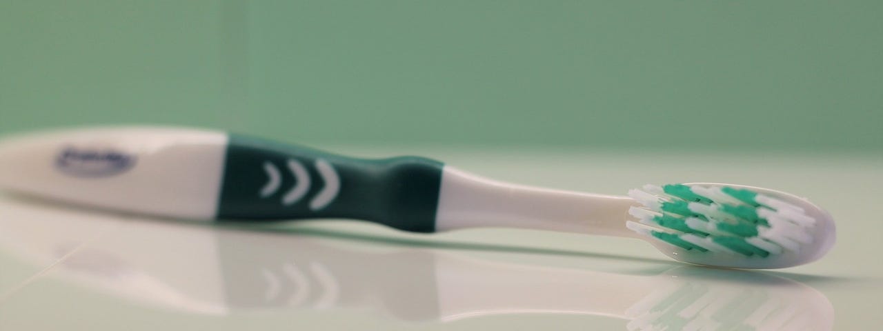 A green and white toothbrush laying on a countertop on its side.