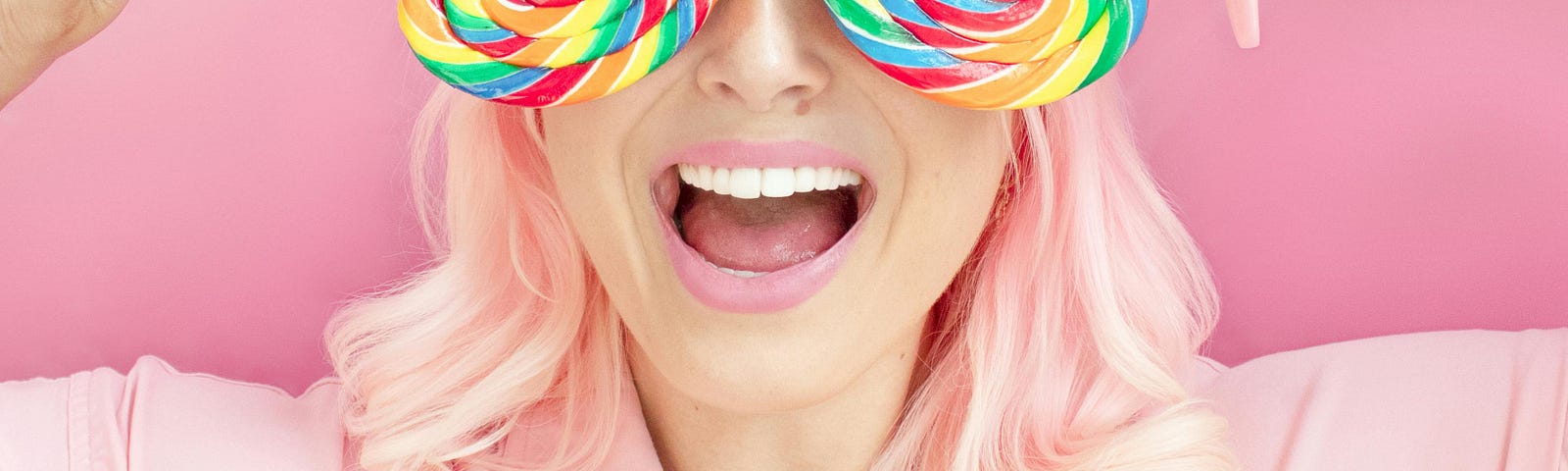 A woman with a pink background, and holding two large heart-shaped lollipops in front of her eyes