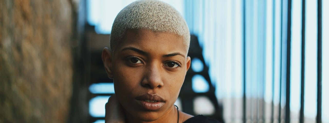 Black woman with short hair with her hand on her neck.