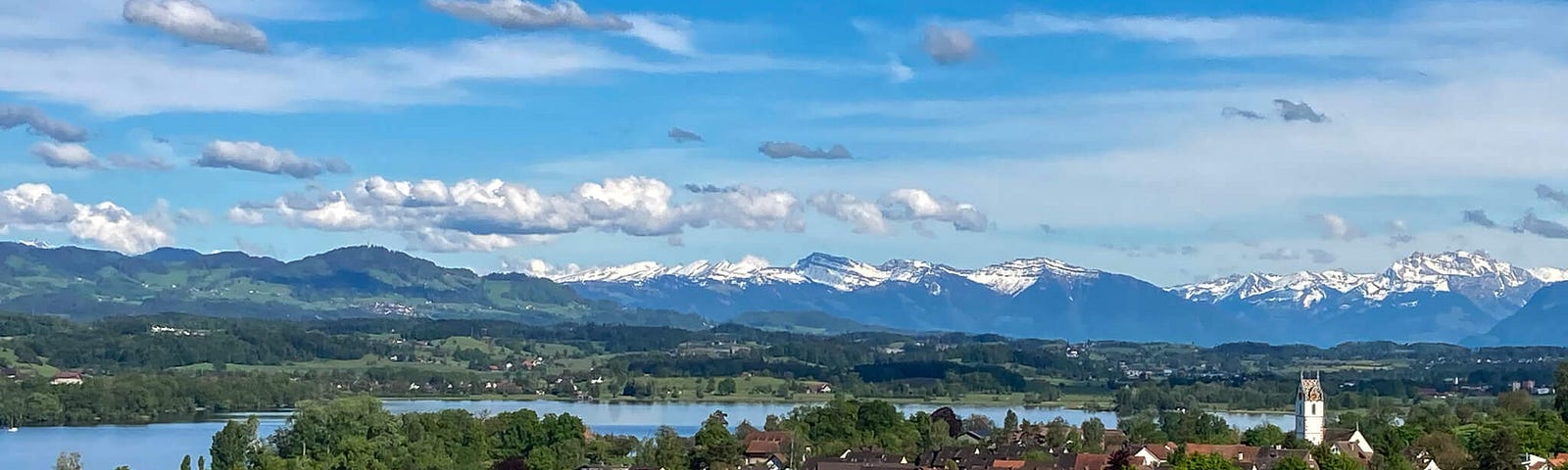 Picturesque Swiss town with green field in foreground and lake and mountains in the background. The wealthy Swiss aren’t as worried about rising sea levels because we have no coastline, only lakes