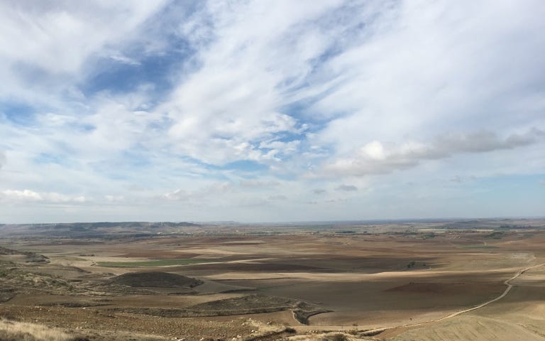 Photo of Camino de Santiago in Spain. A long dirt road with blue sky and clouds above.