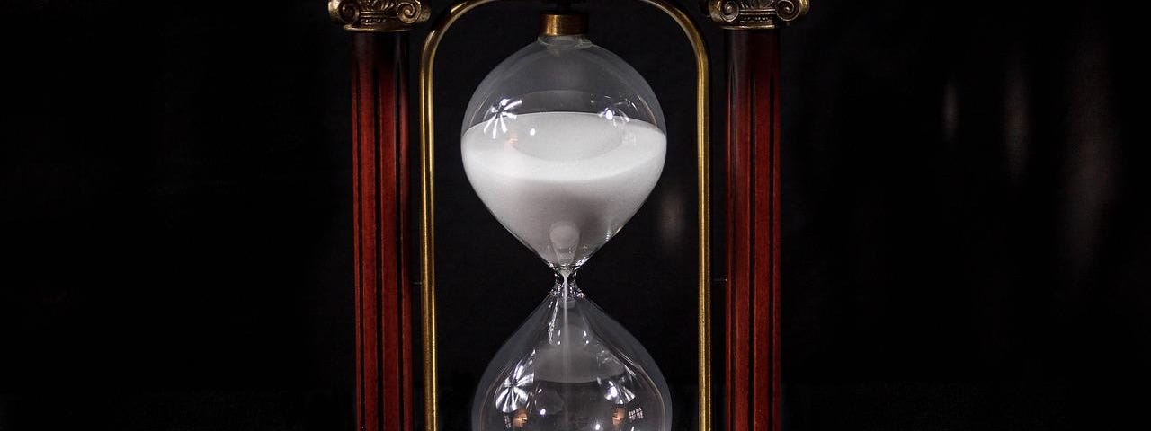 Wooden hour-glass with white sand against a black background.