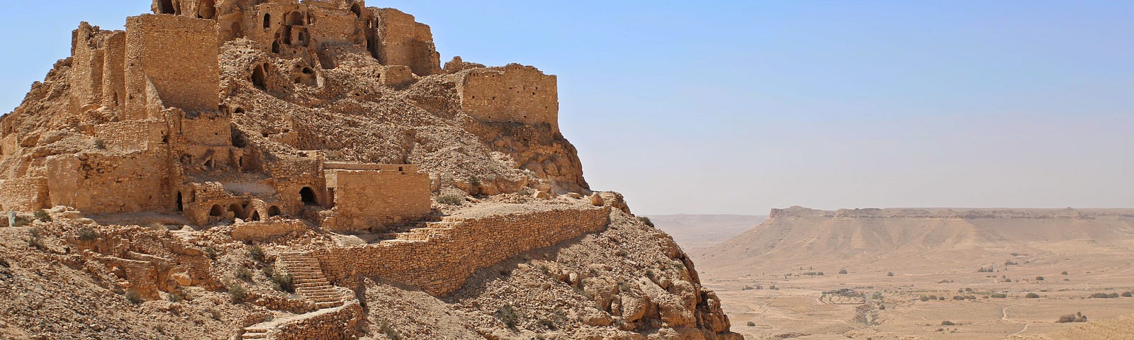 A sandy mountain in Tunisia with a staircase and buildings built into the hillside. All is the same sand colour except for the blue sky.