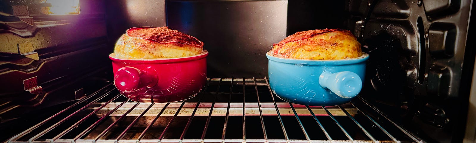 Two French Onion soup bowls in the oven. Cheese soufflé is rising hign above the rim.