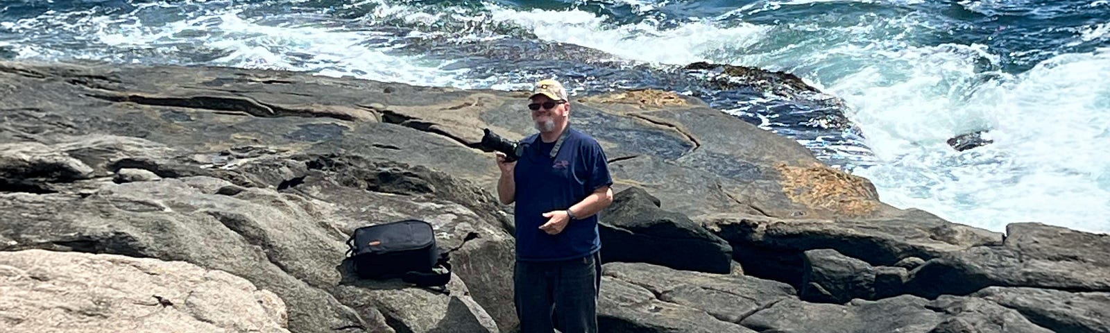 Photograph of a man standing on the rocks near the shore.