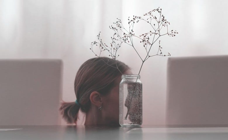 A woman looks at herself through a distorted reflection flipped through a small vase.