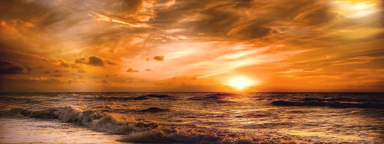 A glorious orange sky over a perfect beach as the sun rises at dawn.