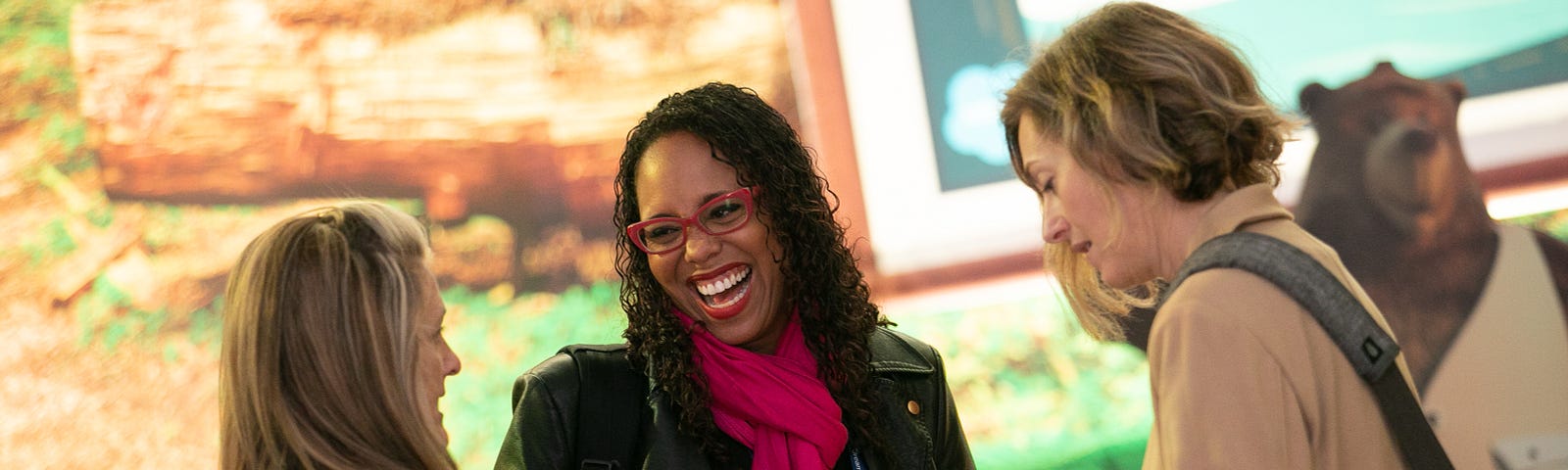 Three women stand together talking and laughing at a recent Salesforce event.