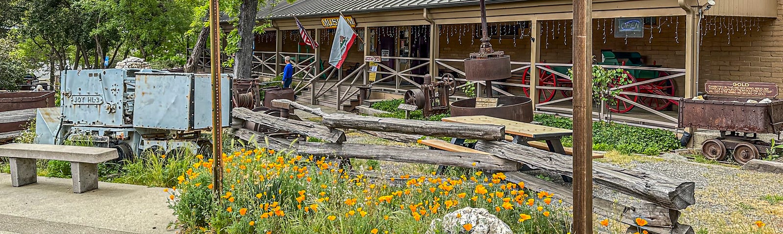 Exhibits of old mining equipment between a row of poppies in the foreground and the front entrance to the museum in the background.