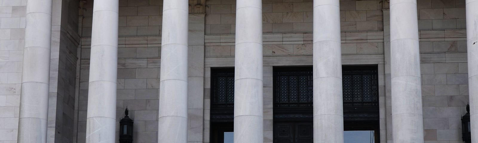 Photo of the sandstone Capitol building, with Judge Yu and the governor talking together while walking down a wide, tall set of steps with the soaring sandstone columns of the building behind them