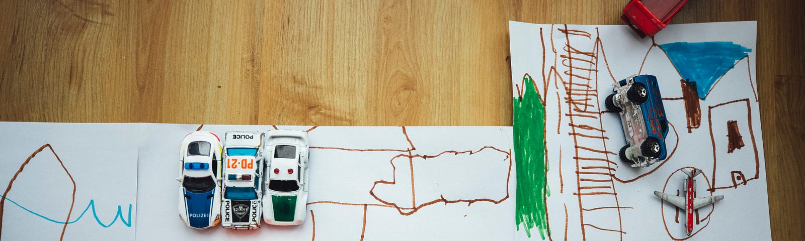 Toy vehicles set up over a child’s drawings of roads.