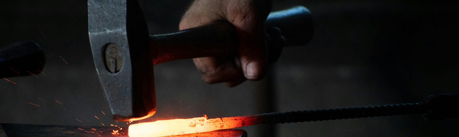 A blacksmith forging metal with hammer and anvil.