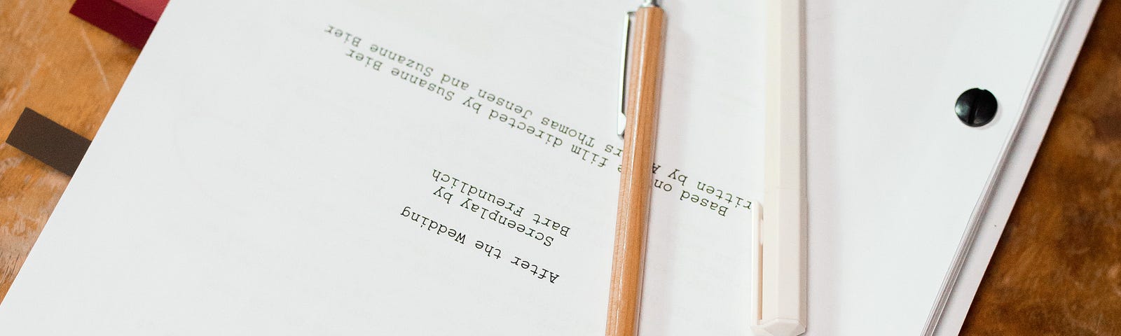 A typewritten manuscript closed on a table with a pencil and pen on top.