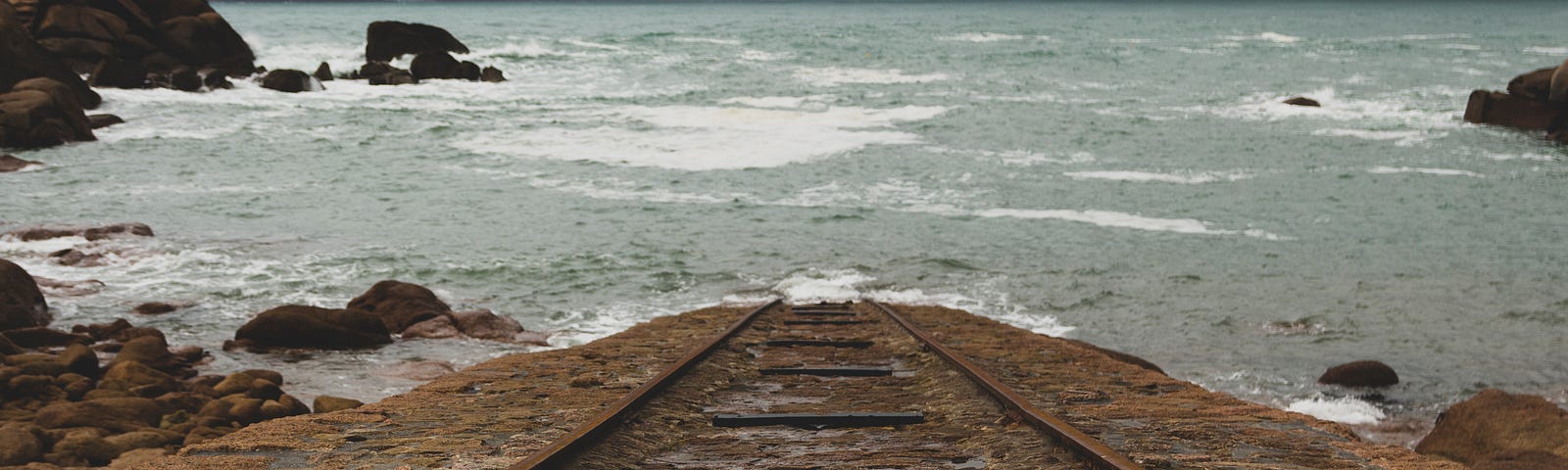 Image of an old railroad track that runs  into a body of water and disappears.