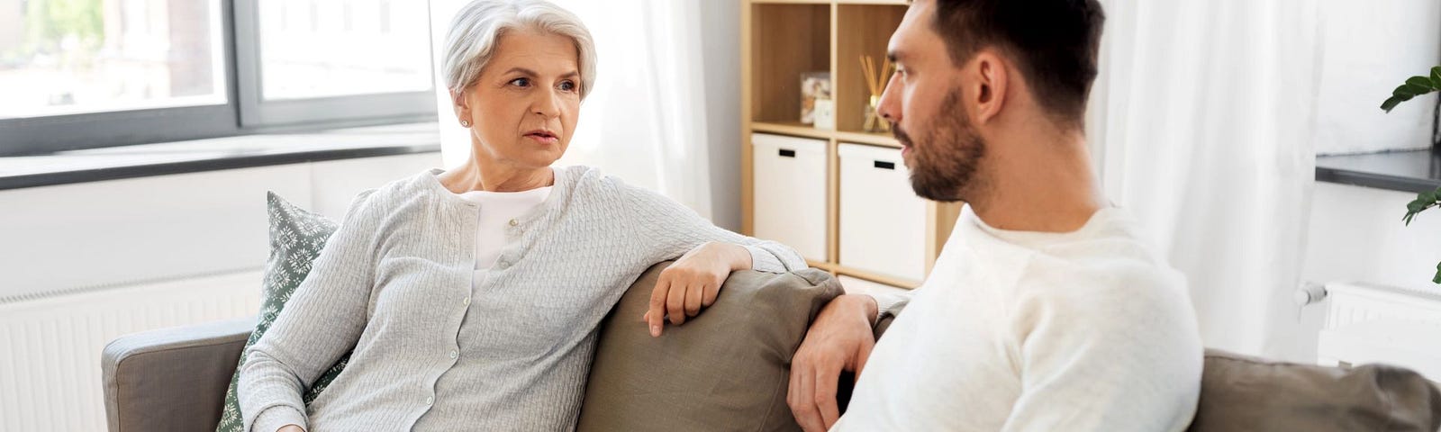 An older woman talks to a younger man on a couch