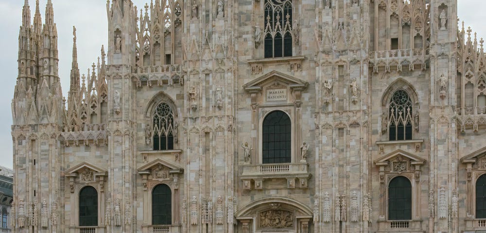 Hundreds of people standing around in the piazza in front of the Milan Cathedral.