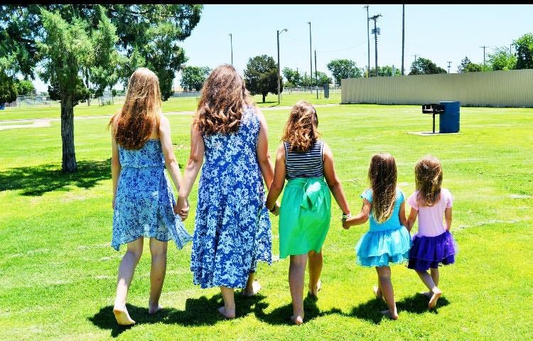 Five girls walking in a park holding hands supportingly, respectfully.