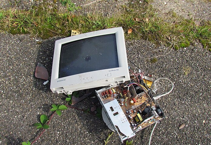 A computer monitor lying smashed to pieces on tarmac.