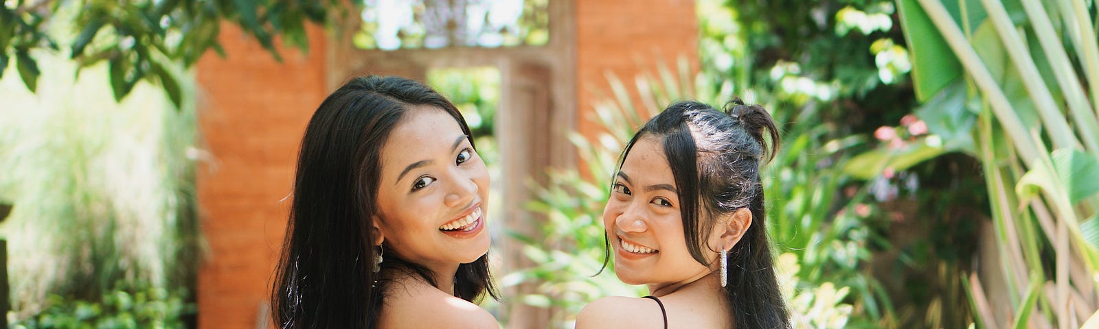 Two women with long dark hair looking over their shoulders toward the camera