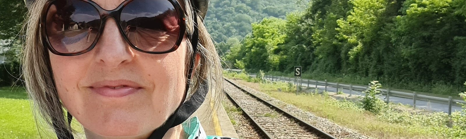 Lisa in front of a railway track in cycling gear. Green Bianchi shirt and silver helmet.