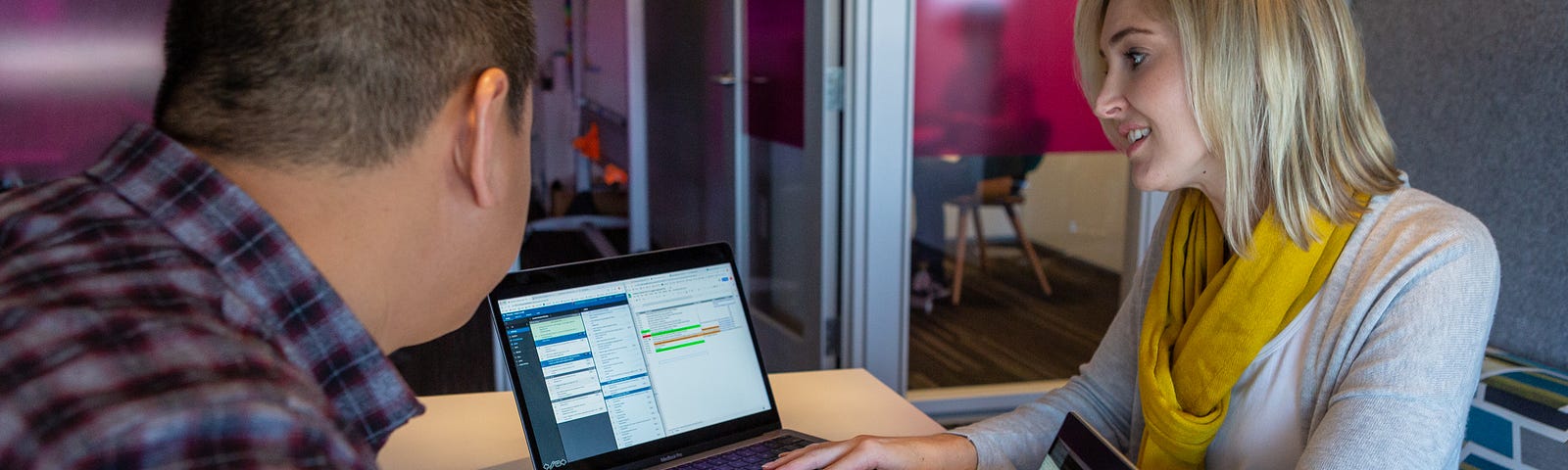 Two employees collaborate on a project on their laptops at a desk