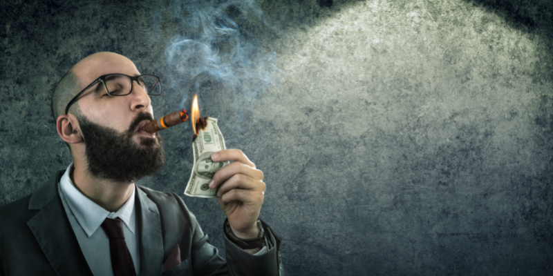 Man with a cigar burning a fake $100 bill — These Article Topics Could Cost You $10,000 and a Year of Blog Growth